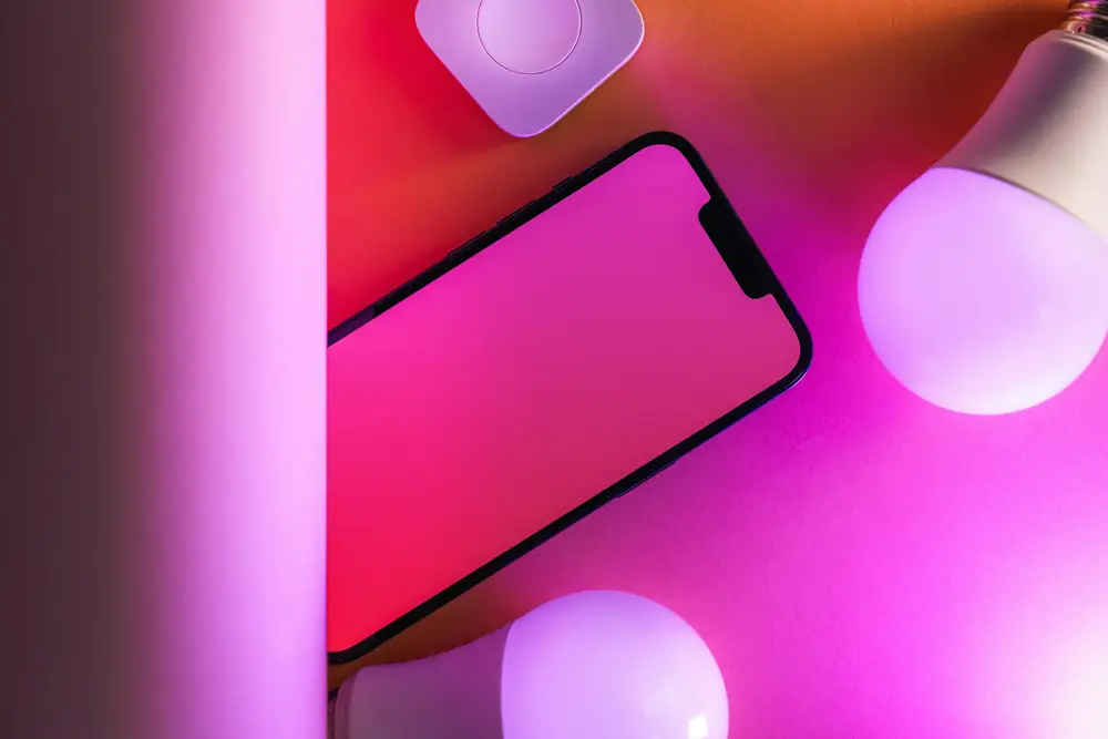 A phone and smart bulbs bathed in pink and orange light