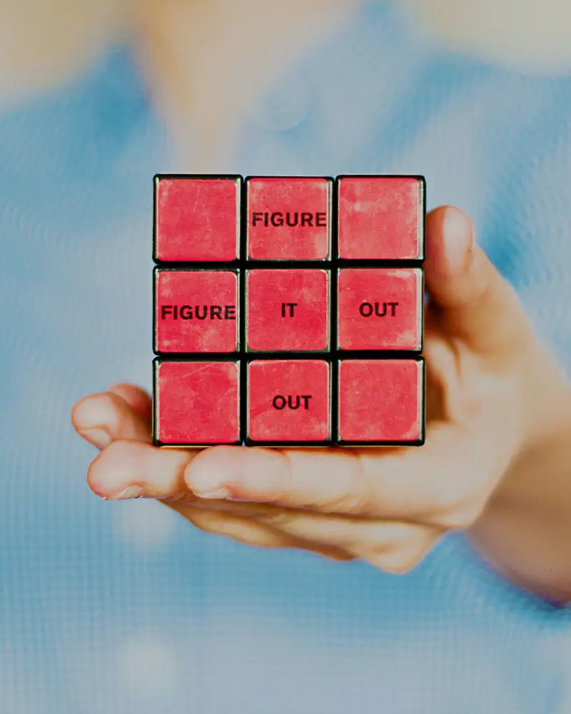 An open hand holding a red puzzle cube printed with the words figure it out