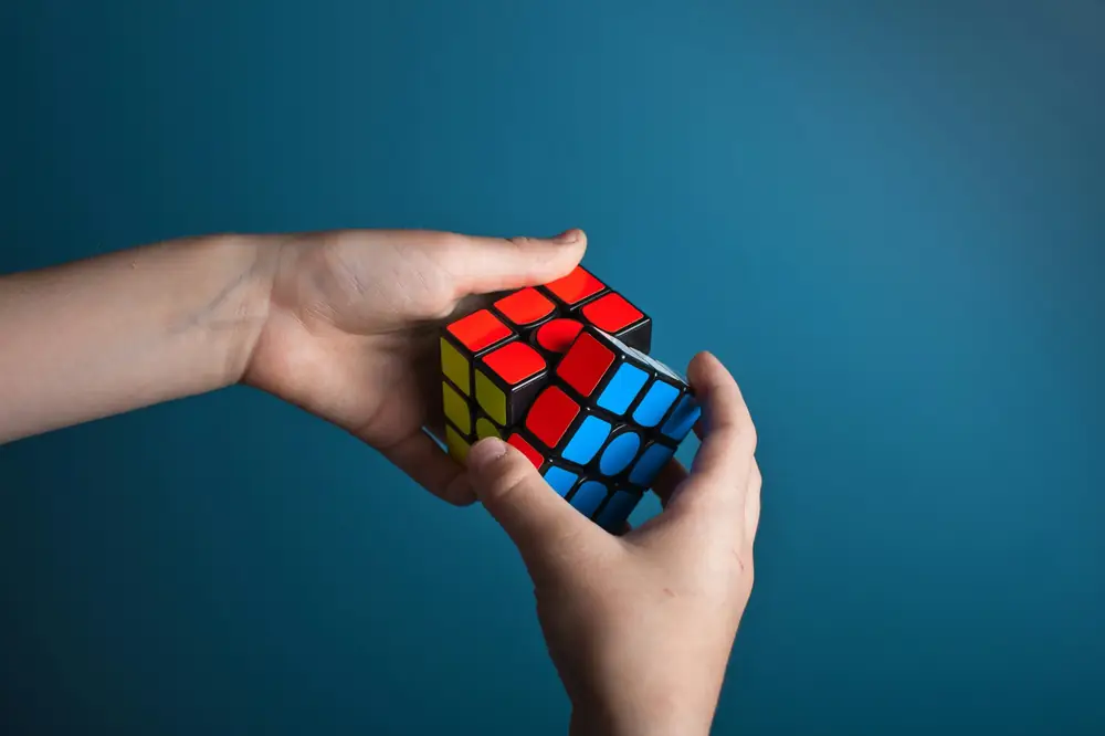 Two hands turning a Rubik’s cube against a blue wall