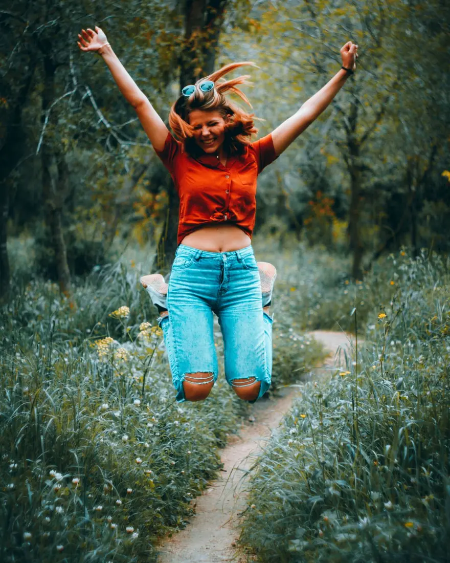A woman leaping with her arms raised on a path through a green meadow