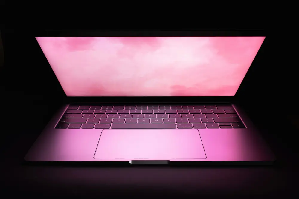An open laptop glowing pink in a dark room